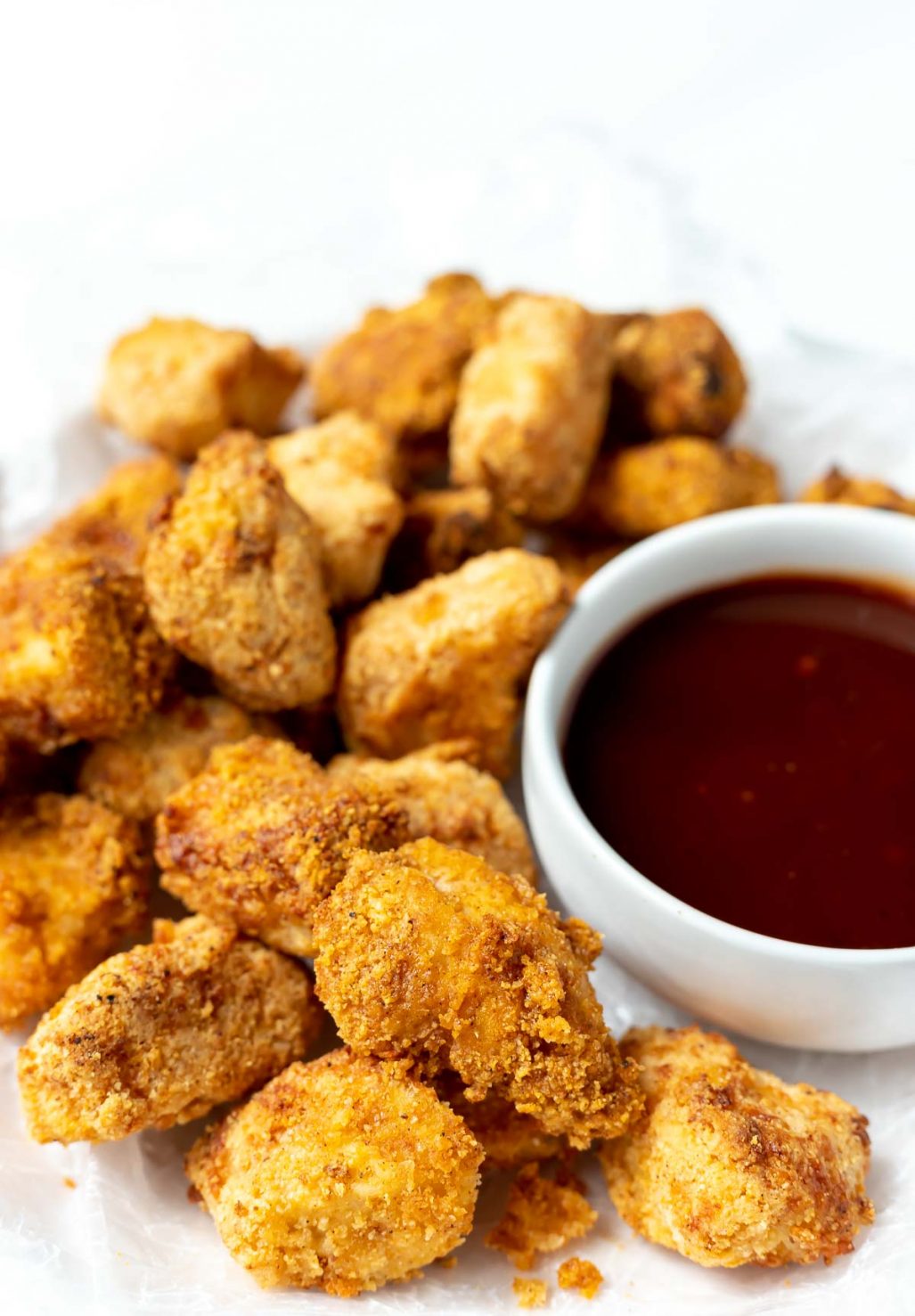 homemade air fryer chicken nuggets on a white plate with barbecue sauce on the side