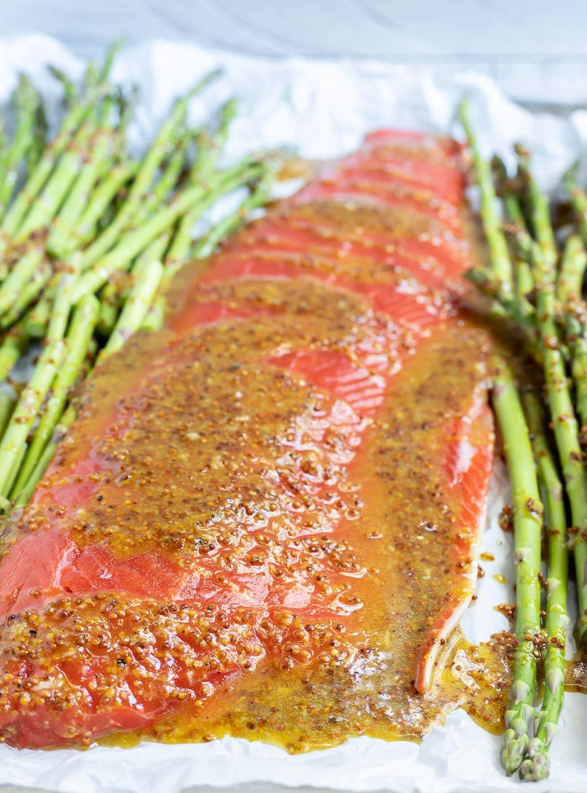 salmon asparagus and sauce on parchment lined sheet pan ready to bake