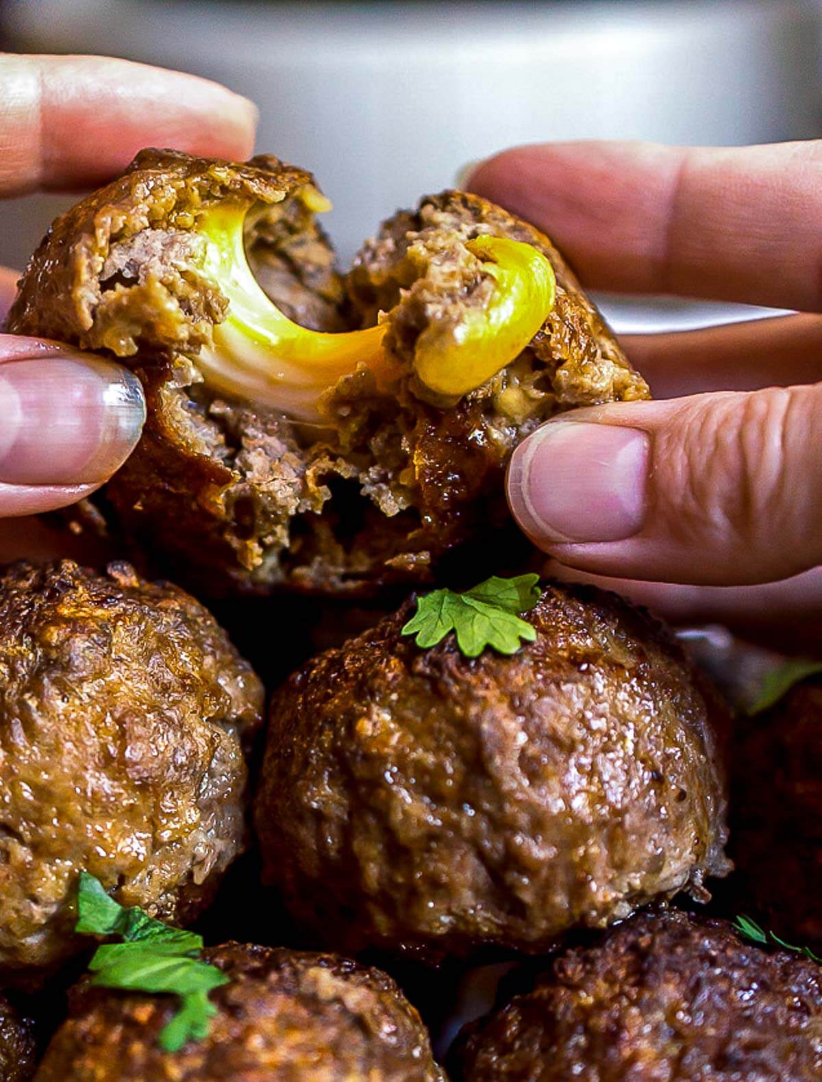 hands pulling apart a stuffed meatball with cheese oozing out