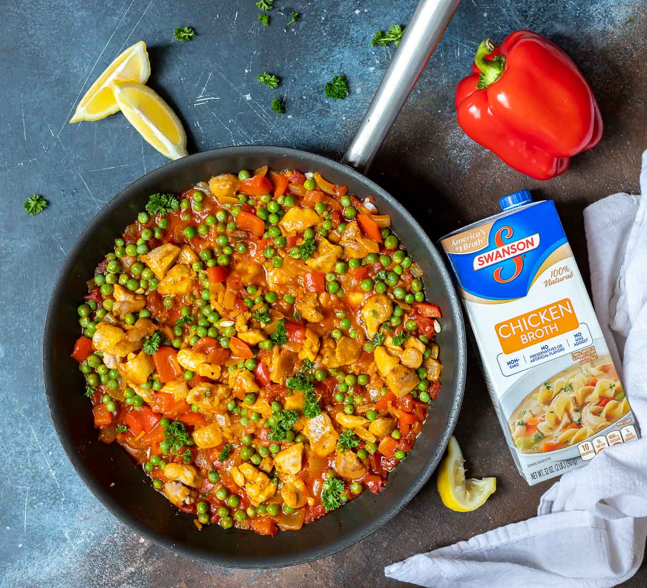 chicken paella in pan with chicken broth container on the side