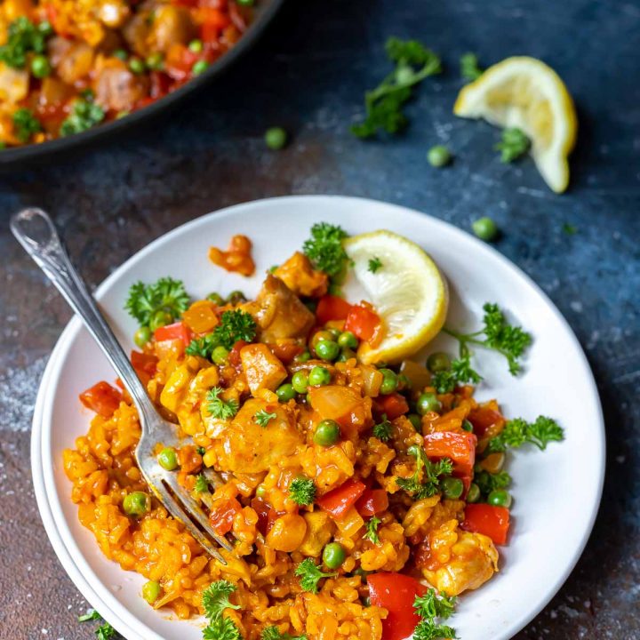 chicken paella served on a white plate with lemons on the side