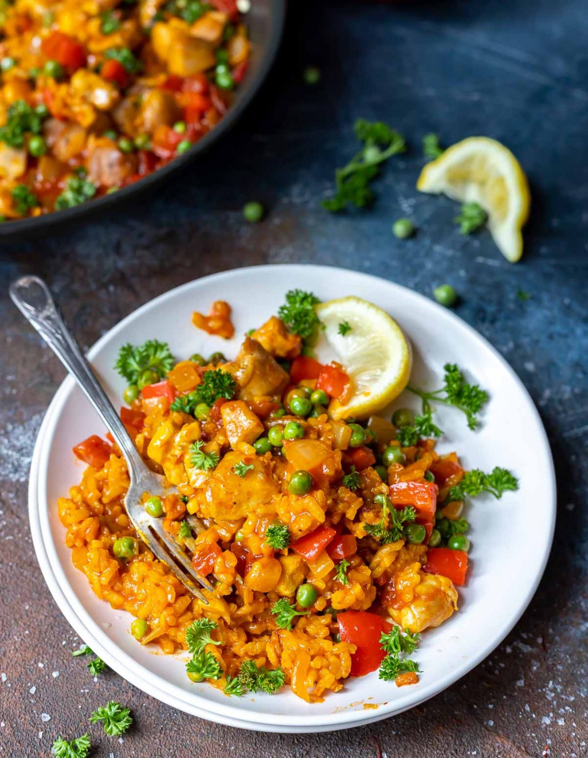 chicken paella served on a white plate with lemons on the side