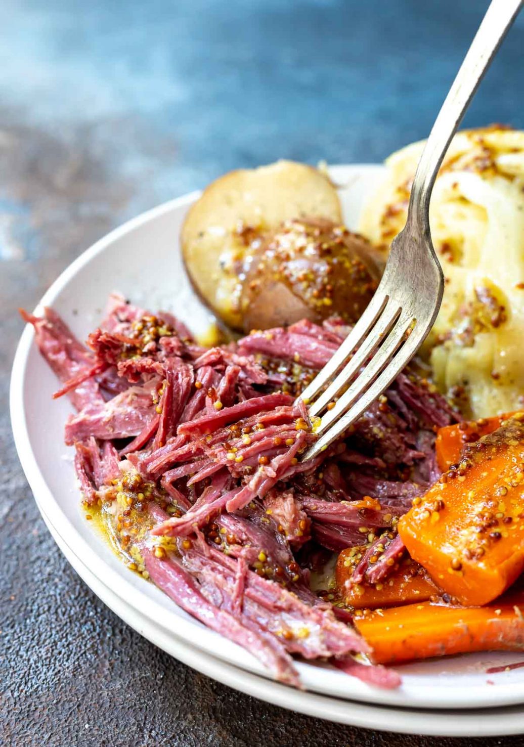 white plate with silver fork picking up crockpot corned beef