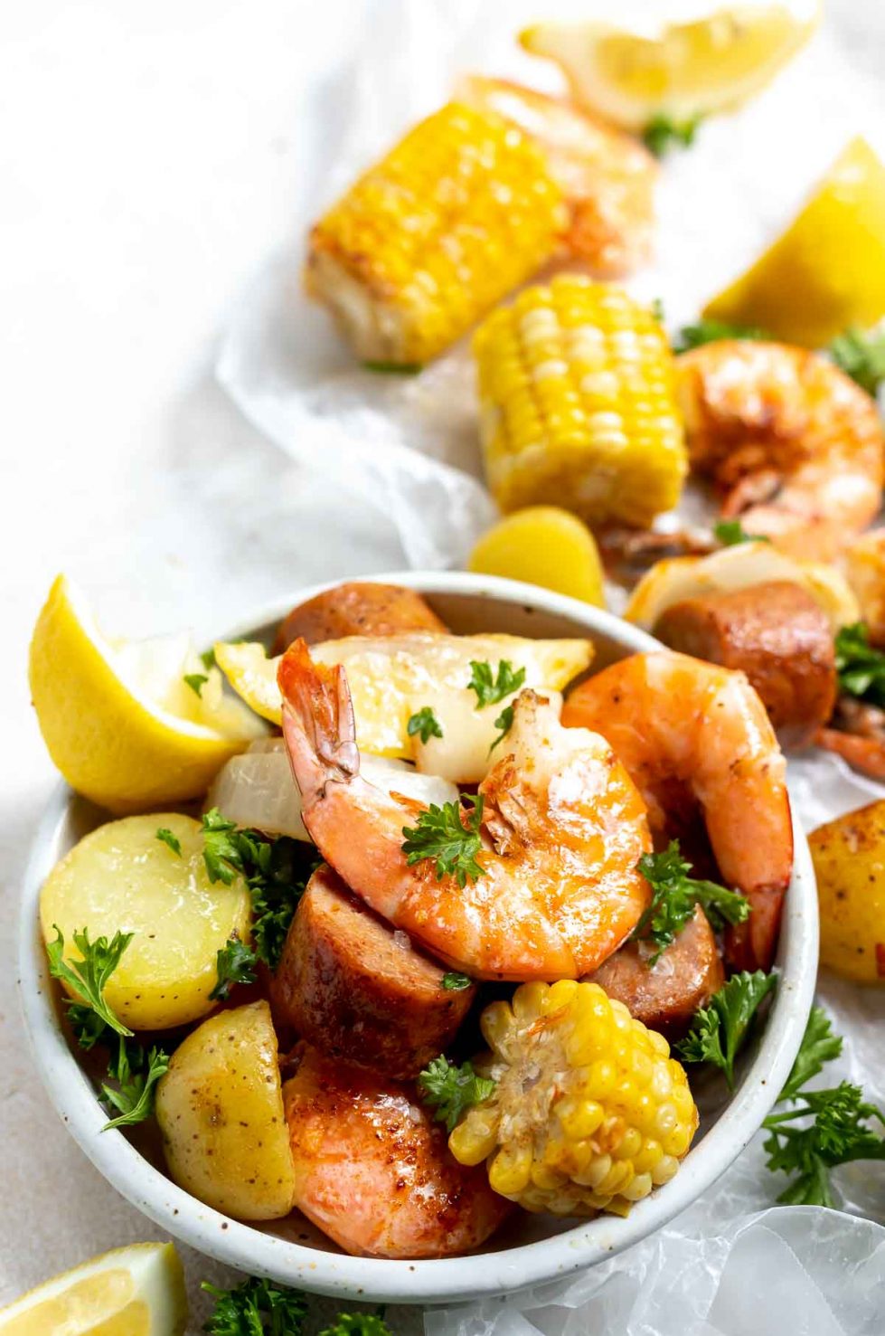 sheet pan shrimp boil shrimp, corn, potatoes, sausage and lemons in a white dish