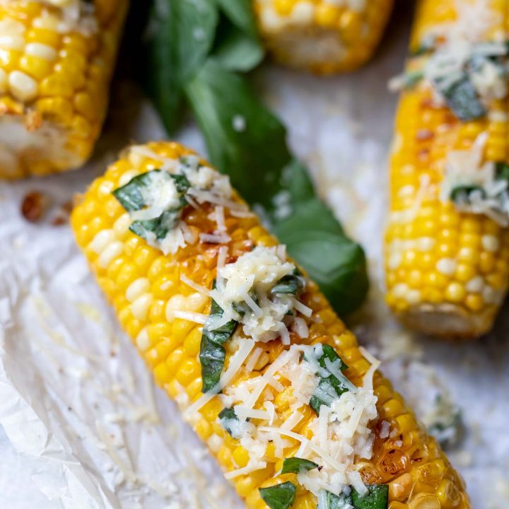 oven roasted corn on the cob topped with butter, parmesan cheese and fresh basil