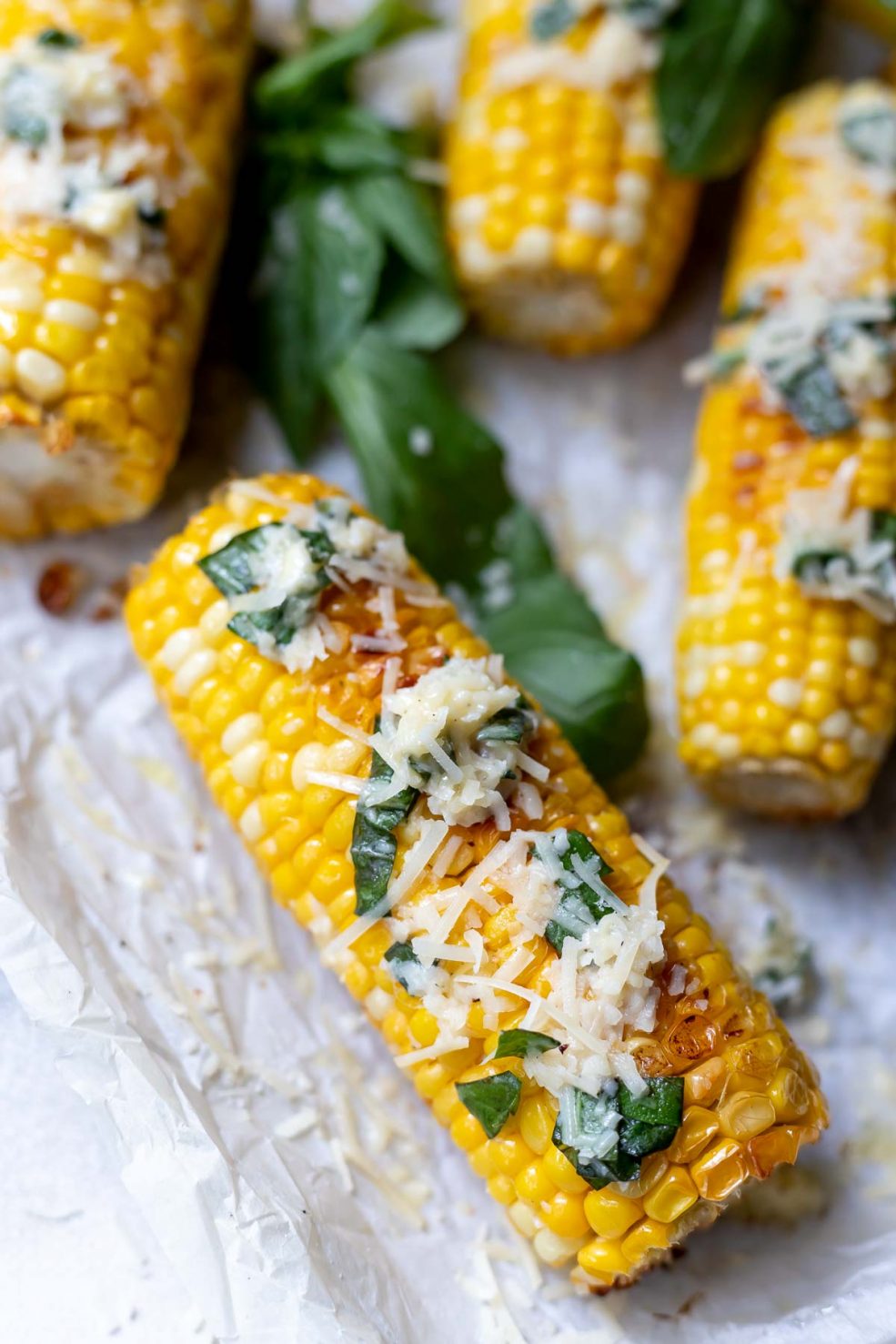 oven roasted corn on the cob topped with butter, parmesan cheese and fresh basil