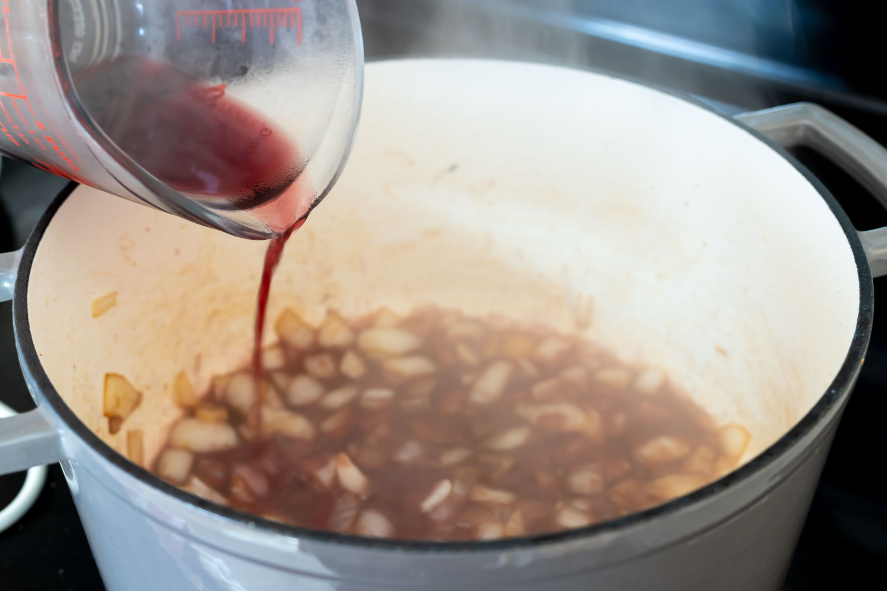 red wine being poured over sautéed onions