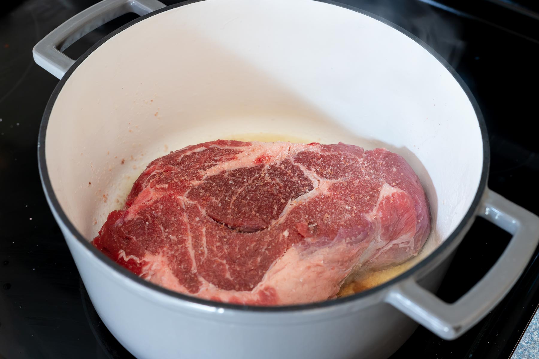 roast being seared in large grey dutch oven on the stove