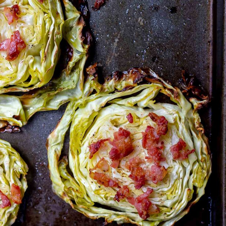 roasted cabbage steak topped with bacon on a dark baking sheet