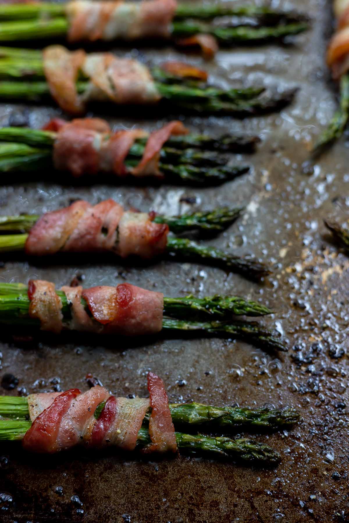 asparagus wrapped in bacon on rimmed baking sheet