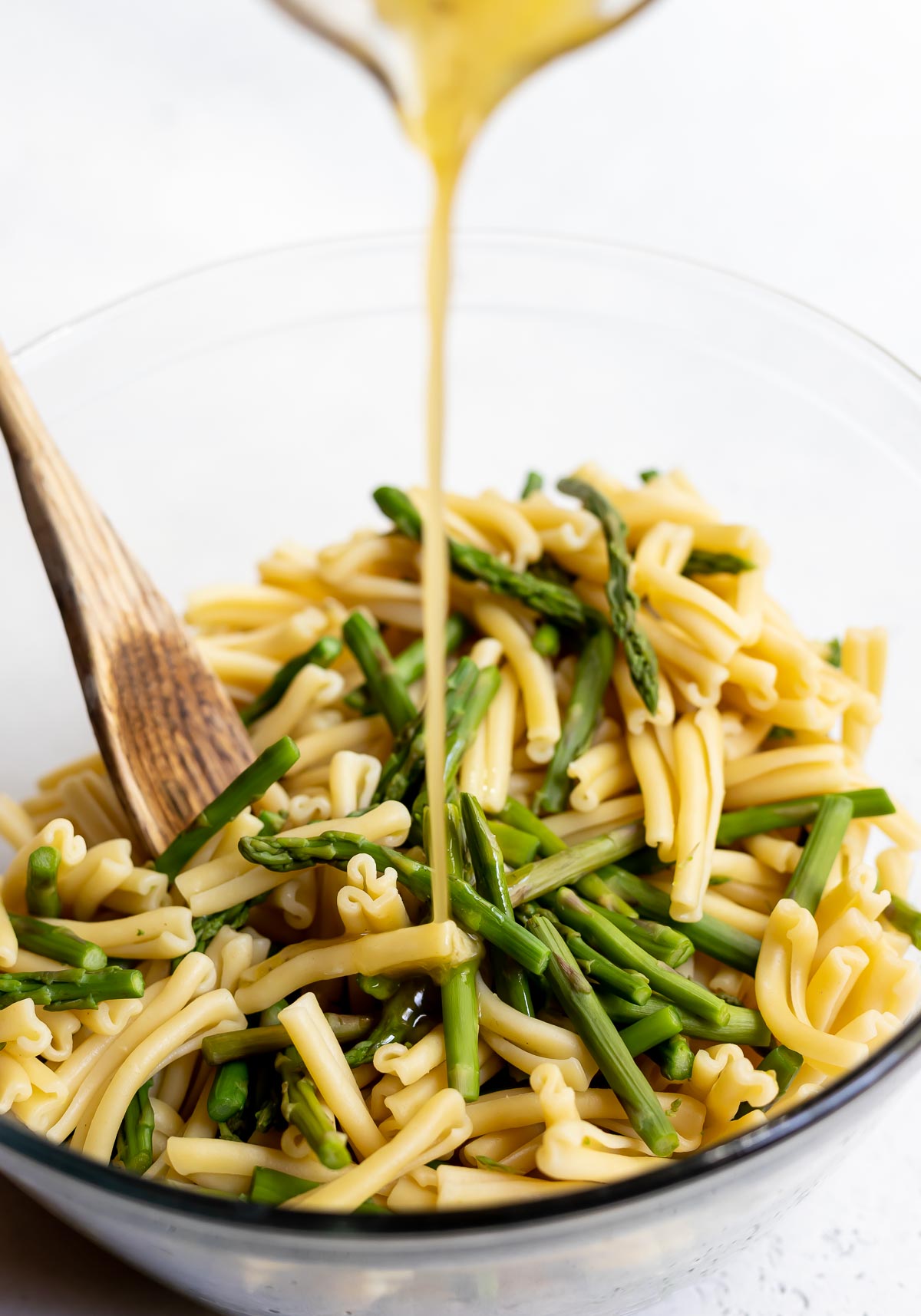 dressing being poured over pasta salad