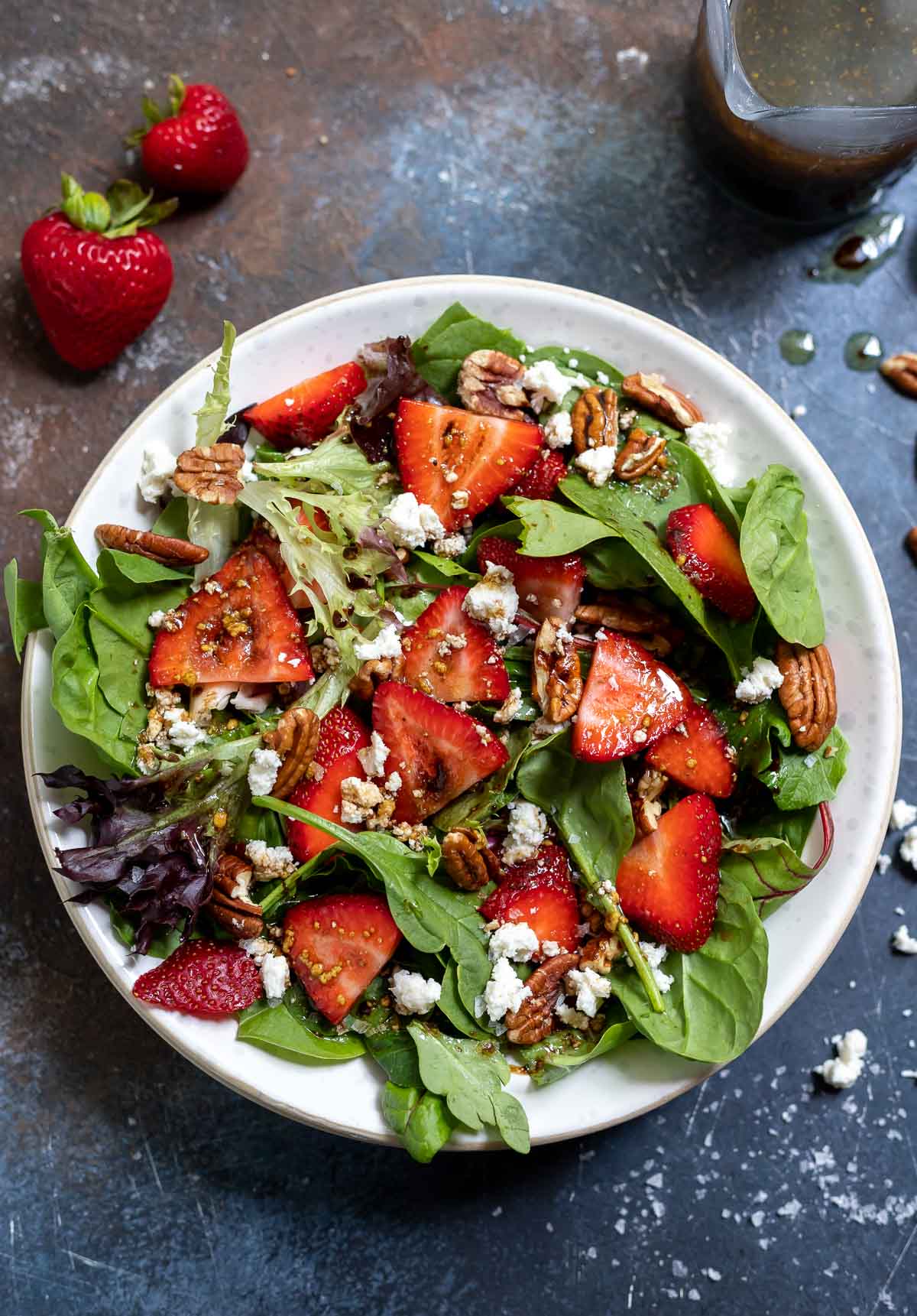 spinach and strawberry salad in white bowl with strawberries on the side