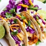 fish tacos topped with mango coleslaw on white plate