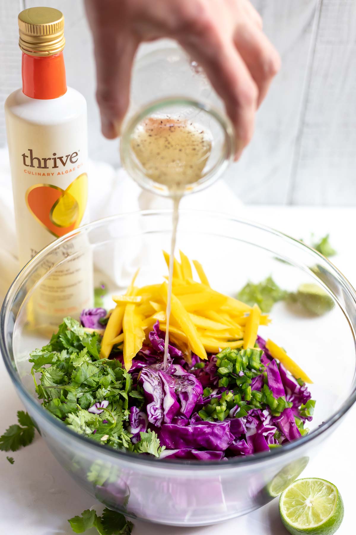 hand pouring dressing over mango cabbage coleslaw