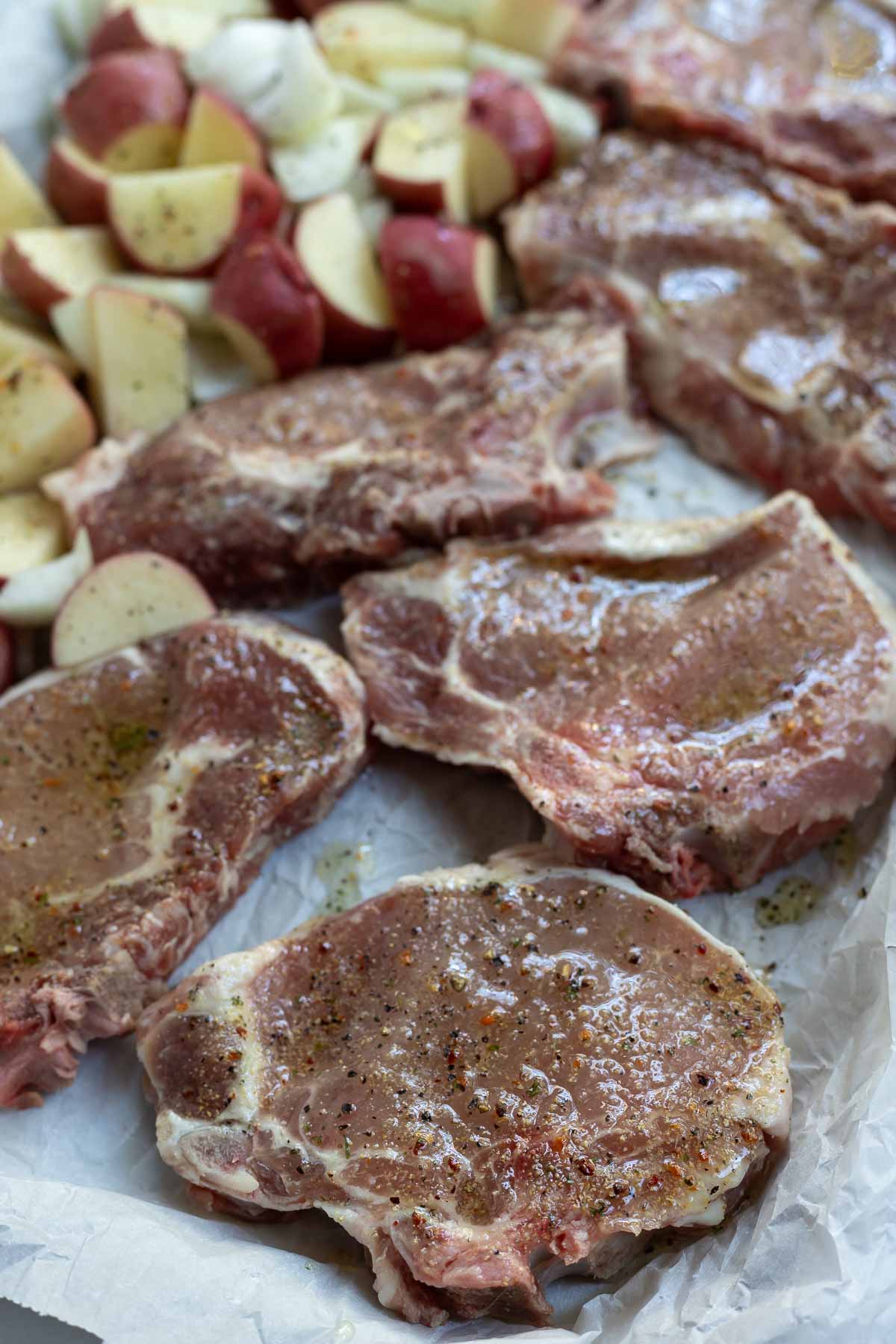 raw seasoned pork chops and potatoes on sheet pan