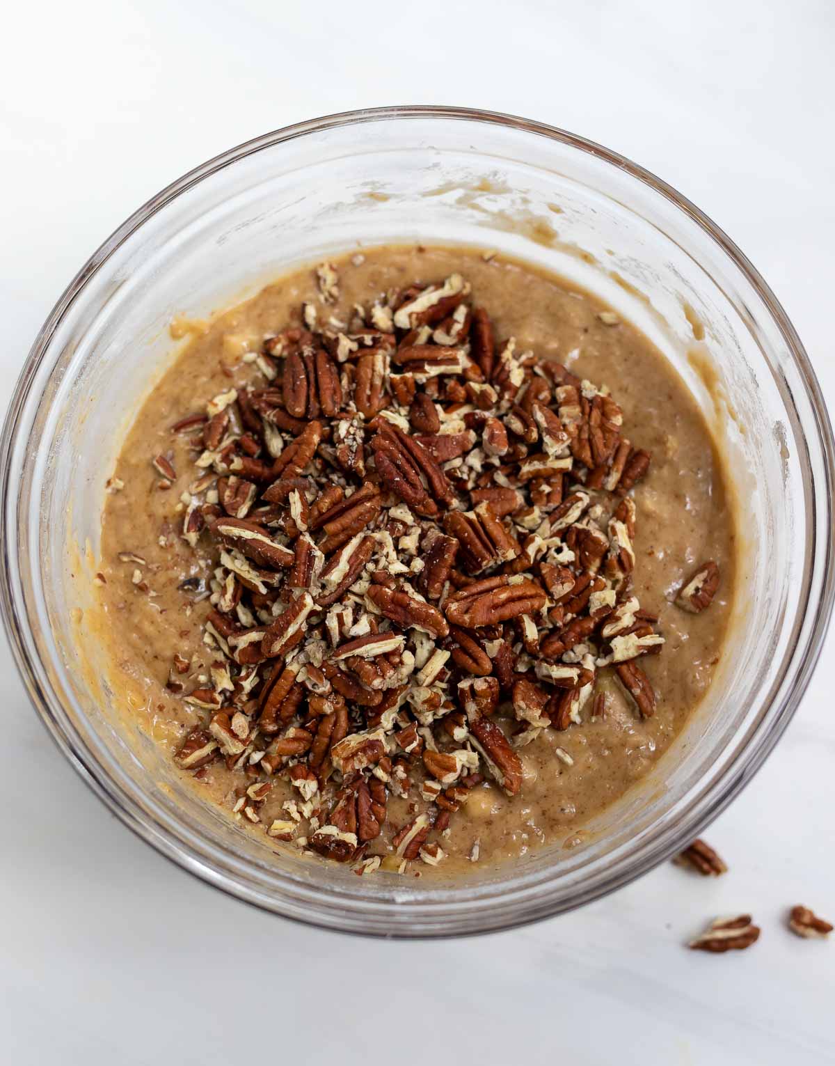 batter topped with chopped pecan in clear glass mixing bowl