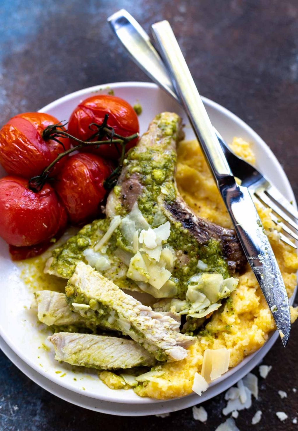 sliced pork chops over polenta and roasted tomatoes on white plate