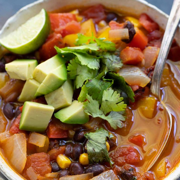 enchilada soup topped with avocado and cilantro in white bowl