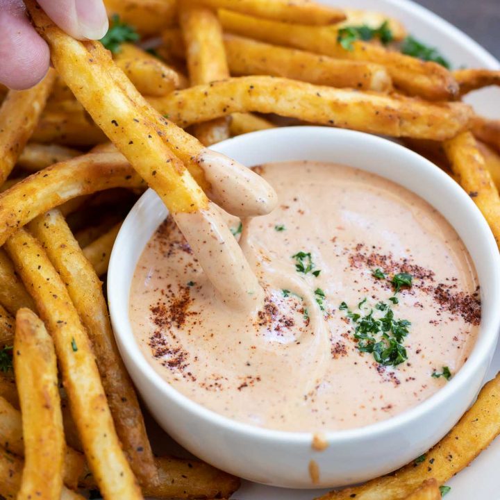 hand dipping golden French fries into secret sauce