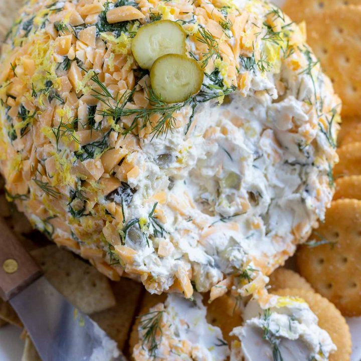 cheese ball coated with pickles, dill and cheddar cheese served next to crackers