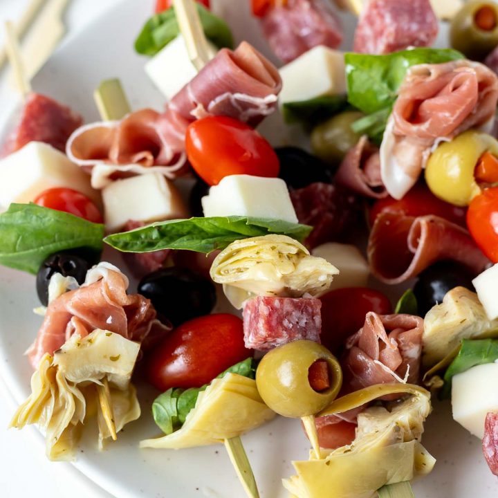 meat, cheese, olives and tomatoes on skewers served on white plate