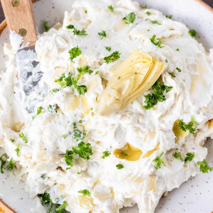 artichoke dip served in white bowl with spreading knife