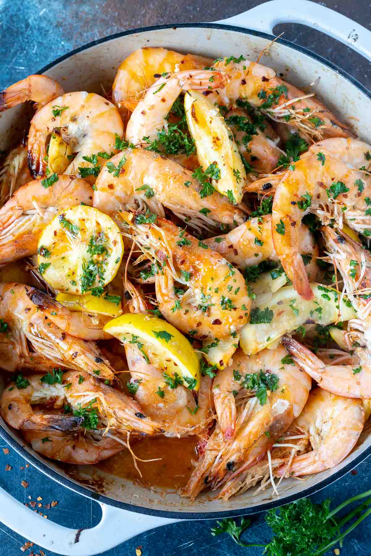 Cooking whole shrimp is quick and easy. This Head On Shrimp Recipe keeps the flavors and process simple and approachable. Whole peel and eat shrimp swimming in a buttery garlic sauce. #shrimprecipes #dinnerrecipes #wholeshrimp #peelandeatshrimp cooked shrimp, lemon wedges and sauce in white pan