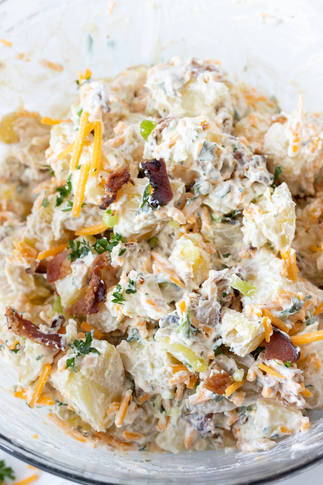 This Loaded Baked Potato Salad Recipe has all the great baked potato topping combined into a flavorful potato salad. Cheese, bacon, sour cream and green onions make this a truly unforgettable side dish. #sidedishrecipes #potatosaladrecipes #loadedpotatosalad potato salad ingredients mixed together in clear glass bowl
