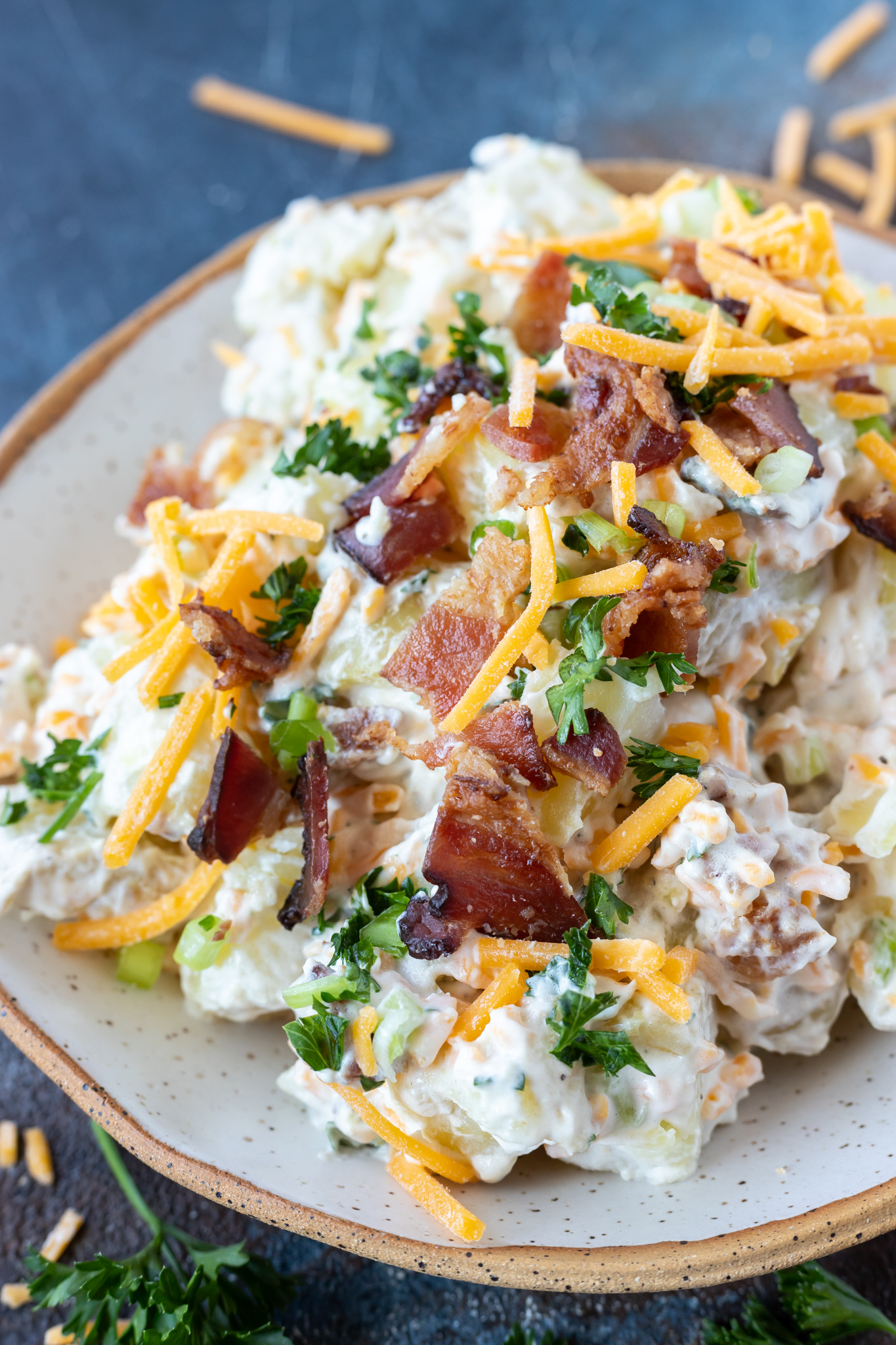 This Loaded Baked Potato Salad Recipe has all the great baked potato topping combined into a flavorful potato salad. Cheese, bacon, sour cream and green onions make this a truly unforgettable side dish. #sidedishrecipes #potatosaladrecipes #loadedpotatosalad potato salad topped with shredded cheese, bacon and parsley served in white bowl