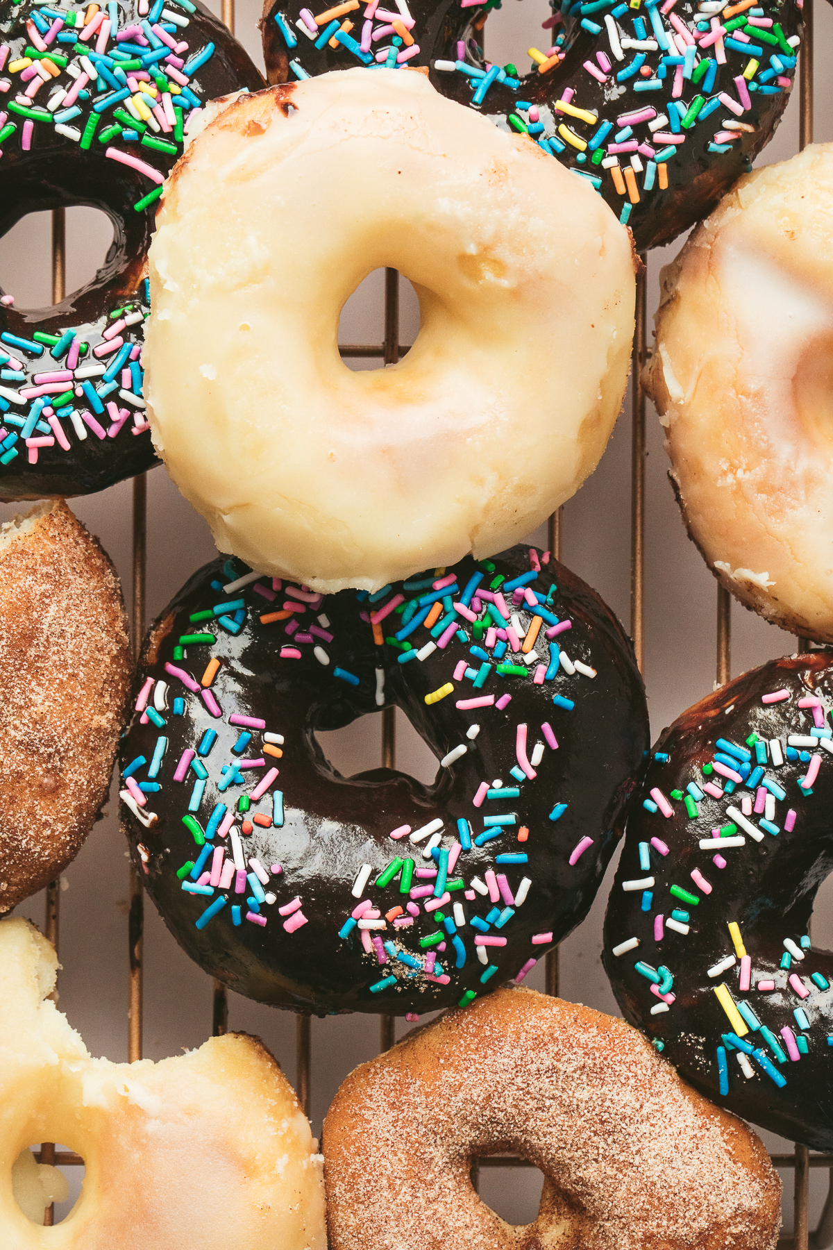 vanilla, chcocoalate glazed and cinnamon sugar donuts on rack