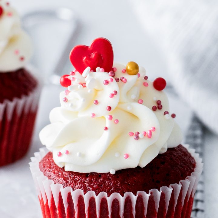 red cupcake topped with white frosting and sprinkles