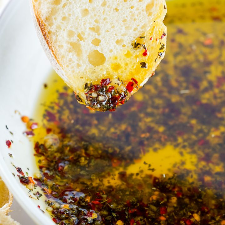 hand dipping bread into oil and herbs