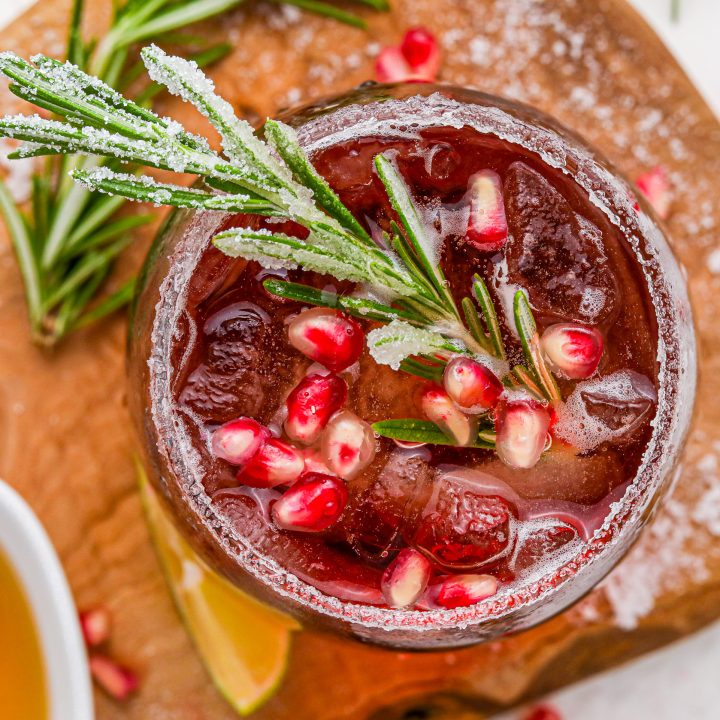 burgundy drink in glass topped with pom seeds and rosemary