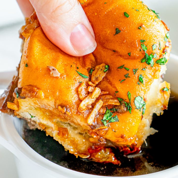 hand dipping sandwich into au jus