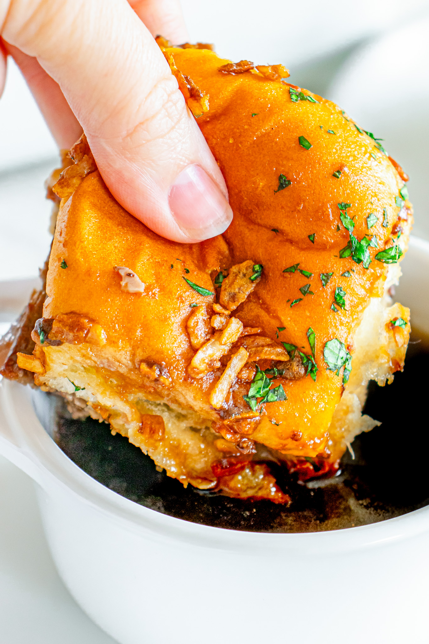 hand dipping sandwich into au jus